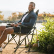 Man sitting comfortably in the indigo RoadTrip Rocker by a lakeside trail.