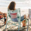 Woman sitting on a green Beach Rocker Chair at the beach, facing the water.