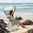 Woman sitting on a green Beach Rocker Chair with a Sunshade Accessory, using her phone.
