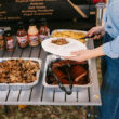 GCI Slim-Fold Table Person serving barbecue from trays on a slim-fold table at an outdoor gathering.